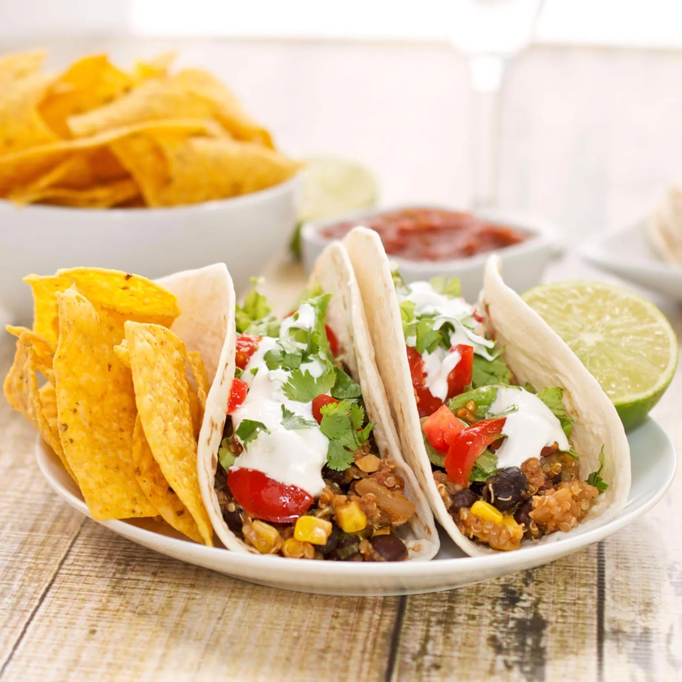 Two soft tacos topped with tomato, cilantro and crema, served with tortilla chips, salsa and lime